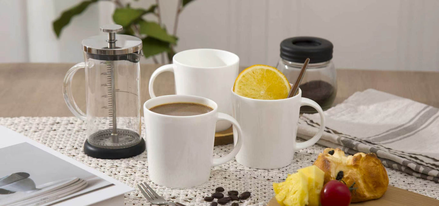 White mugs with coffee, a French press, and breakfast items on a table.