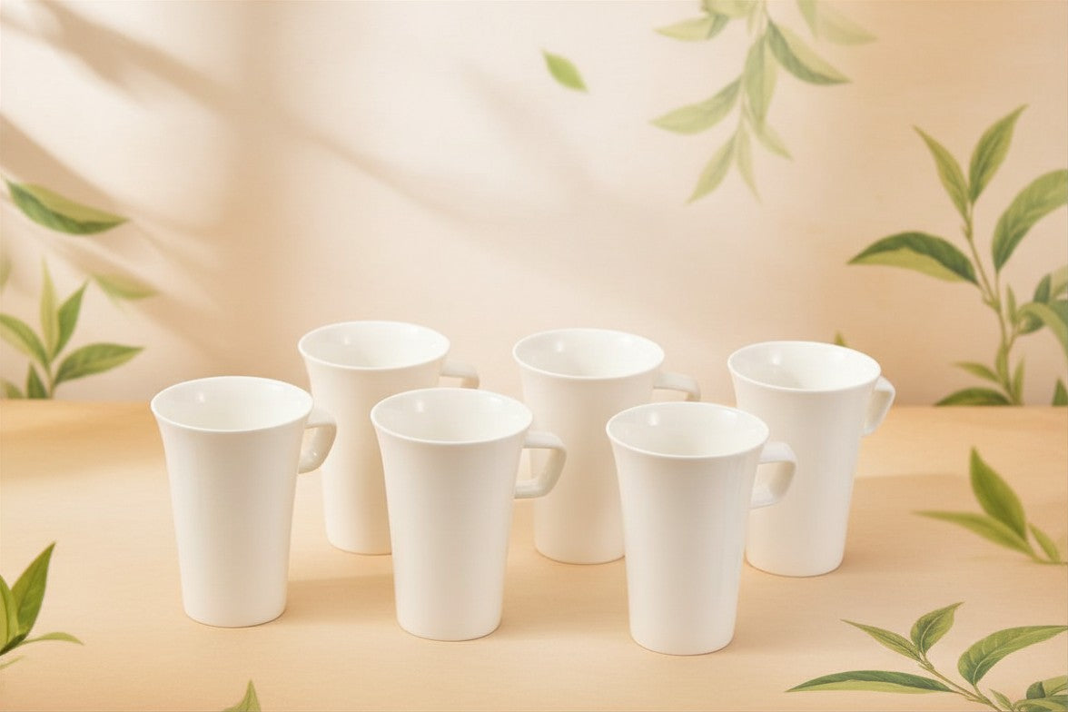 Set of six white ceramic cups on a beige surface with green leaf patterns.