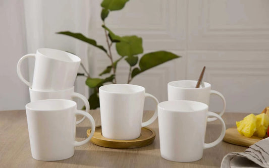 Set of white mugs on a wooden table with a plant in the background