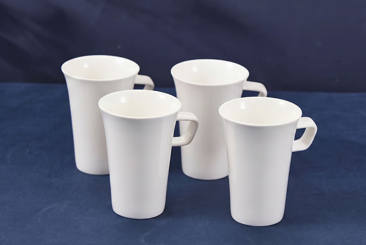 Four white ceramic mugs on a blue background