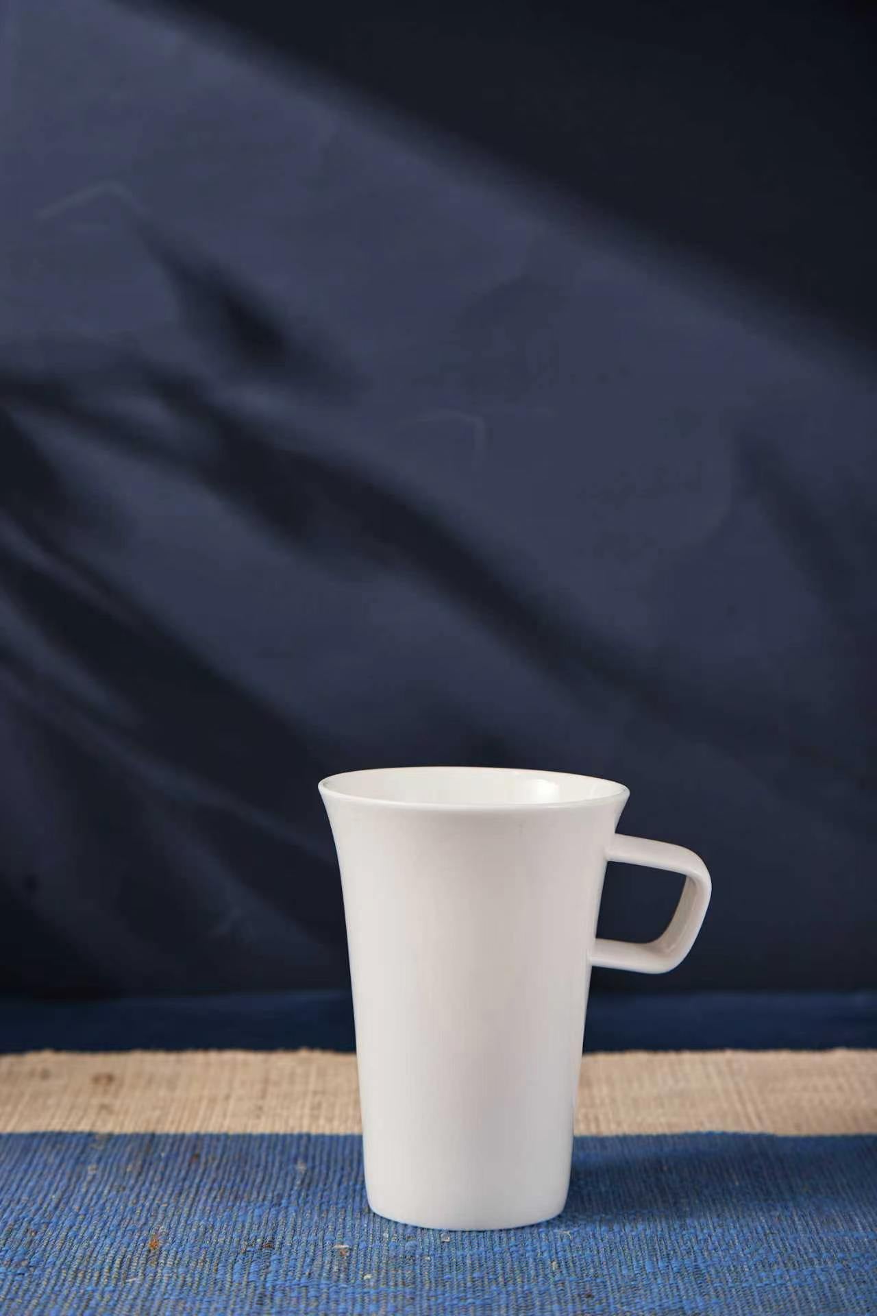 White ceramic mug on a blue textured surface with a dark blue fabric background