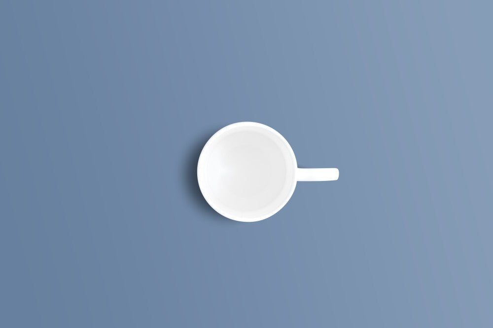 A minimalist white ceramic cup with a handle, shown from a top-down perspective on a solid slate blue background.