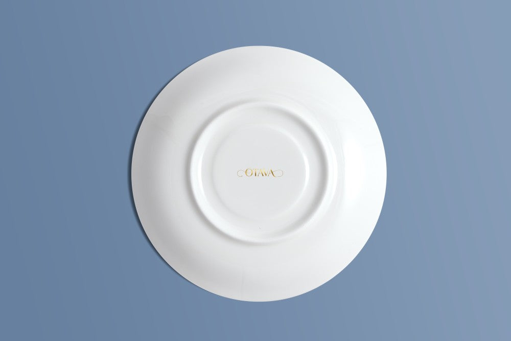 Bone china saucer viewed from above, with the Otava mark in gold at the centre.