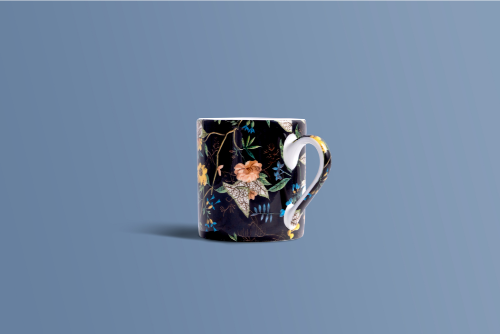 A ceramic mug with a dark navy floral pattern and a sculptural, curved handle, set against a solid slate blue background.