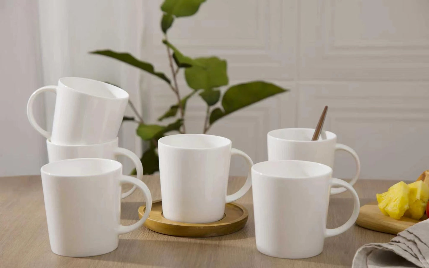 Set of white mugs on a wooden table with a plant in the background